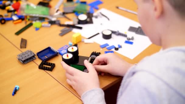 Primer plano, las manos de los niños sostienen un pequeño robot multicolor, máquina, ensamblado de un diseñador. los niños son aficionados a la robótica, programación, modelado , — Vídeo de stock