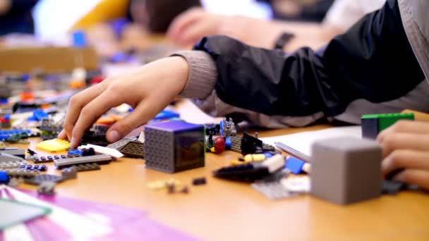 På bordet finns utspridda många detaljer från childrens designer, kuber, ledningar, styrelser, hjul, mångfärgade små robotar, maskiner. barn är förtjust i robotteknik, programmering, modellering, — Stockvideo