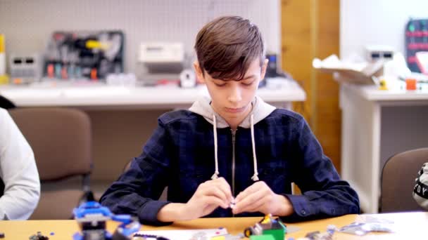 El muchacho de 12 años, juega en el diseñador de cubos, platos, circuitos, cables. un pequeño inventor crea robots, máquinas de diferentes partes del diseñador — Vídeos de Stock