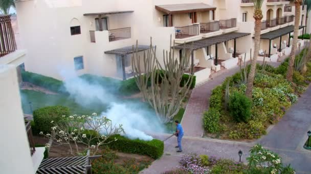 SHARM EL SHEIKH, EGIPTO - 5 DE ABRIL DE 2018: Hotel Jaz Belvedere. El hombre trabaja empañándose para eliminar los mosquitos con una máquina de humo especial. nubes de humo blanco suben — Vídeos de Stock