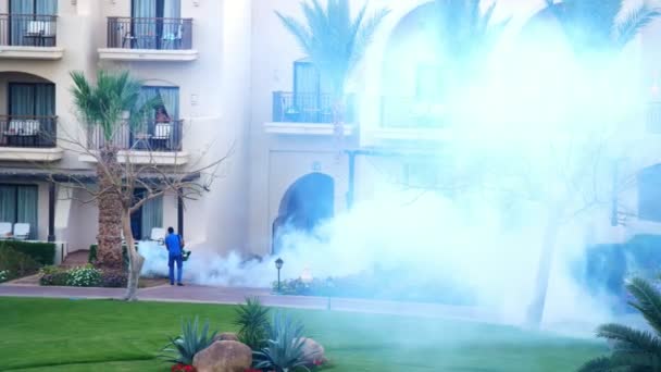 SHARM EL SHEIKH, EGITO - 5 de abril de 2018: Hotel Jaz Belvedere. O homem trabalha embaçando para eliminar mosquitos com uma máquina de fumaça especial. nuvens de fumaça branca subir — Vídeo de Stock