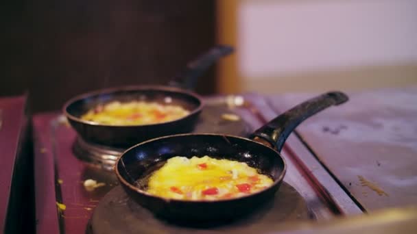 Omeletes, ovos fritos, cozidos no fogão em duas panelas gordurosas e sujas. O fogão também está sujo. sobre as panelas você pode ver uma fumaça leve — Vídeo de Stock