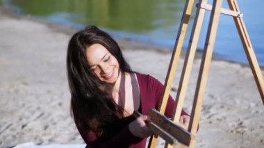 nehir kıyısında plaj. Şafakta, güzel bir kadın sanatçı bir şövale iş için hazırlar. gülümsüyor.