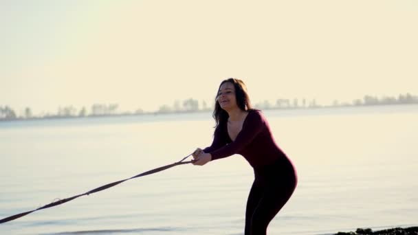 On the river bank, on the beach. at Sunrise , a beautiful woman in a tight suit walks with a dog of Husk breed, keeps the dog on a leash, plays with a dog, has fun. summer — Stock Video