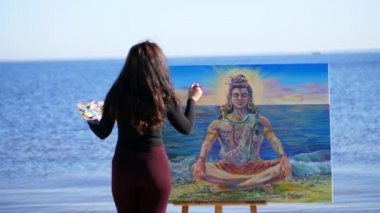 Yaz, sahilde Nehri yakınında. güneş doğarken, dar elbiseli güzel kadın sanatçı bir resim çizer. Tanrı Shiva resimde tasvir