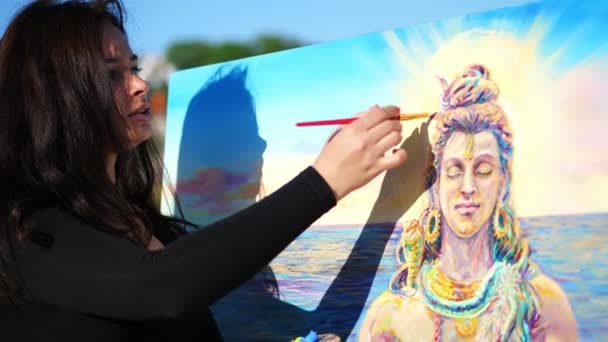 Zomer, buitenshuis, in de buurt van de rivier, een mooie vrouw kunstenaar is tekenen, verven op canvas met een speciale kleine spatel, is van toepassing met behulp van een speciale tekening techniek. houdt van een palet met verf — Stockvideo