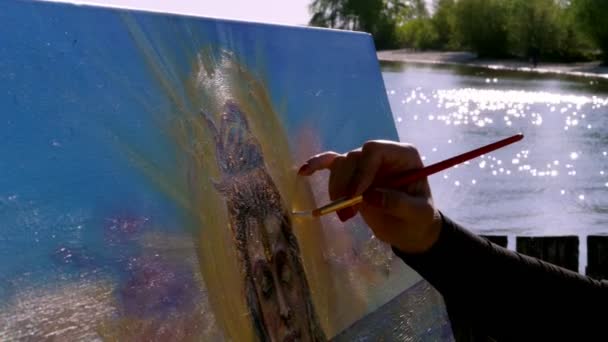 Verano, cerca del río, en la playa. al amanecer, una hermosa artista sostiene un pincel en su mano, dibuja un cuadro. pinta sobre lienzo al dios Shiva . — Vídeos de Stock