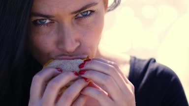 Yaz, açık havada. cinsel hamburger ısırma güzel esmer kadın, koyu saçlı, fastfood, yeme aralıyor portresi. O tombul dudakları var.