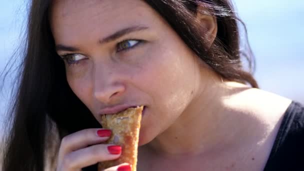 Plage de mer. portrait de belle femme, aux longs cheveux foncés, avec apétite manger tarte à la confiture de cerises avec thé. pique-nique en plein air, meilleur petit déjeuner — Video