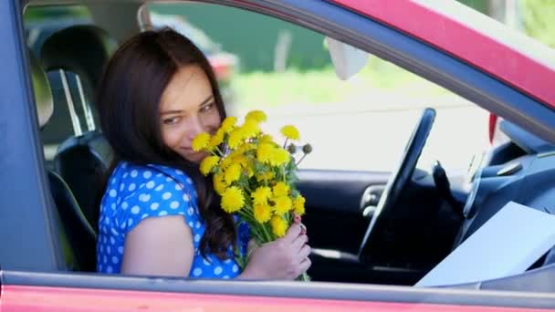 Wanita berambut cokelat cantik duduk di dalam mobil, dengan karangan bunga dandelion kuning. tersenyum. Musim panas — Stok Video