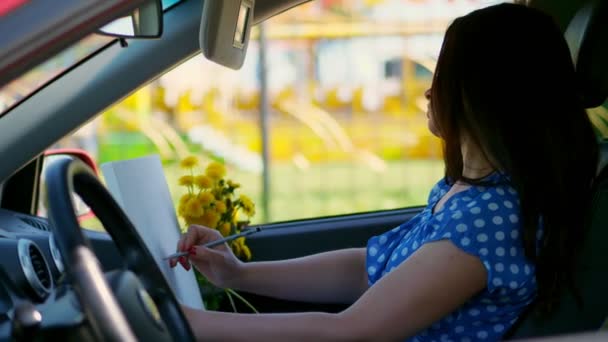 Künstlerin, schöne brünette Frau, sitzt im Auto, zeichnet Bleistiftskizze, zeichnet Strauß gelben Löwenzahns. Zeichnung aus der Natur, der kreative Prozess des Zeichnens. Sommer — Stockvideo