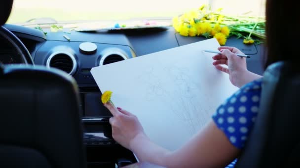 Kunstenaar, mooie brunette vrouw, zit in de auto, trekt potloodschets, tekening boeket van gele paardenbloemen. tekening van de natuur, het creatieve proces van tekening. zomer — Stockvideo