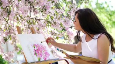 Beyaz elbiseli, sanatçı boya bir resim içinde çiçek açan çiçeklerin güzel kadın ressam bahar elma bahçesi, o bir palet boya ve bir fırça ile onun elinde tutan