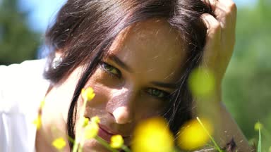 güzel bir esmer kadın, yeşil çim ve sarı çiçekleri ile'nın bahçesinde açık havada portresi. o gülümsüyor, elini saçları ile çalışır, onun kulağına güzel bir küpe görebilirsiniz.