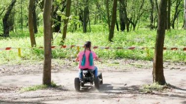 Yaz günü genel pine city Park, parlak pembe tişört ile küçük kız sürme, bir childs sürüş dört tekerlekli motosiklet, mini moto dört, quadricycle pigtails renkli. Çocuklar yaz tatili