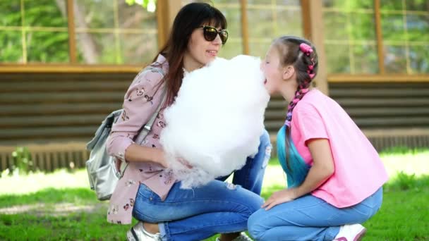 Брюнетка, в солнечных очках, с дочерью, девочкой 8 лет, с голубыми косичками, ест сладкую сахарную вату, свежевыжатую нитку, смеется, веселится, в городском парке, летом — стоковое видео