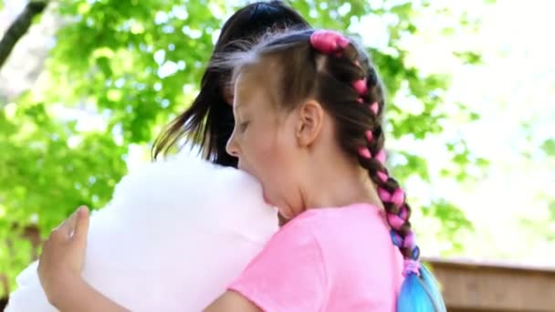 Brunette vrouw, dragen van een zonnebril, met haar dochter, meisje van 8 jaar oud, met blauwe pigtails, eten van zoete suikerspin, candyfloss, lachen, plezier, in stadspark, in de zomer — Stockvideo