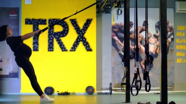 Cherkasy, Ukrayna, 20 Kasım 2019 Trx eğitimi. Geniş göbekli, siyah dar eşofmanlı hamile atletik kadın spor salonunda trx fitness kayışlarıyla egzersiz yapıyor. — Stok video