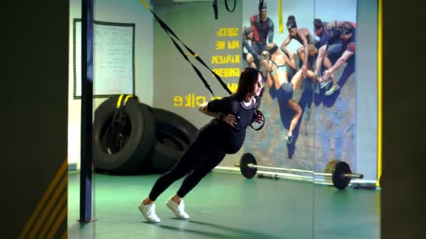 Treino TRX. jovem mulher atlética grávida, com uma barriga grande, em um traje de treino apertado preto, está fazendo exercícios com tiras de fitness trx no ginásio — Vídeo de Stock