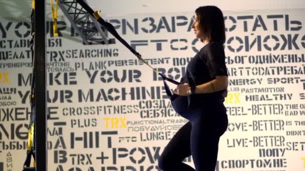 Czerkasy, Ukraina, 20 listopada 2019: Trening Trx. młoda ciężarna sportowiec kobieta, z dużym brzuchem, w czarnym obcisłym dresie, robi ćwiczenia z trx paski fitness w siłowni — Wideo stockowe