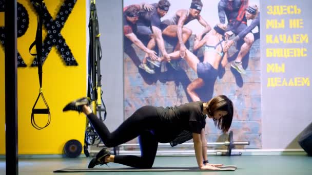 Czerkasy, Ukraina, 20 listopada 2019: młoda ciężarna atletyczna kobieta, z dużym brzuchem, w czarnym dresie, wykonuje ćwiczenia pośladków i mięśni nóg na macie w siłowni — Wideo stockowe