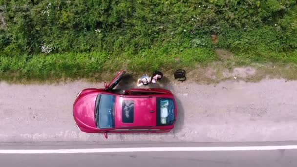 Aero. view from above. a couple of tourists, a young man and a woman in sunglasses, who travel in a red car, waving their hands up a drone, tourists shoot themselves with a drone — ストック動画