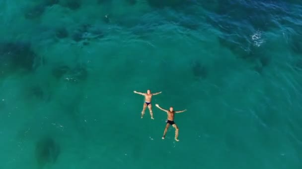 Aero, widok z góry. w turkusowych, błękitnych wodach morza, dwóch mężczyzn pływa, leżą na plecach w postaci gwiazd. lato gorący słoneczny dzień — Wideo stockowe