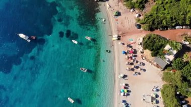 Havacılık. Üst Manzara. Güzel yaz deniz manzarası. Yunanistan 'ın Evia Adası' nın vahşi plajı. Turkuazlı deniz bölmesi, dağların eteğinde mavi su. Tatilciler plajda güneşleniyor, bir sürü şemsiye var.,