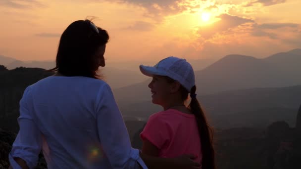 Umrisse einer Frau und eines Mädchens im Teenager-Alter vor dem Hintergrund des Sonnenuntergangs in den Bergen. Touristen bewundern den Sonnenuntergang im Meteora-Gebirge, Griechenland, im Sommer. — Stockvideo