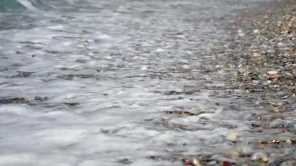 Gros plan. vagues douces, avec de la mousse blanche sont lavés à terre, sur la plage de galets. beaux cailloux ronds multicolores sur la côte méditerranéenne, rivage. journée chaude d'été. Grèce — Video