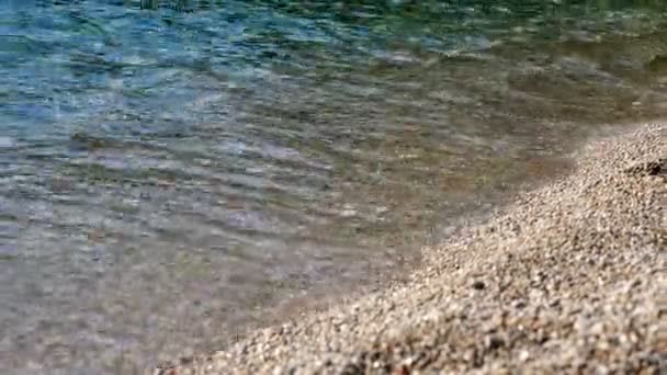 Nahaufnahme. Weiche Wellen mit weißem Schaum werden an den Kieselstrand gespült. schöne, mehrfarbige runde Seekiesel an der Mittelmeerküste, Küste. Sommerlich heißer Tag. Griechenland — Stockvideo