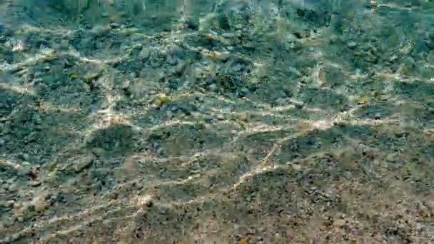 Close-up. sob a água clara do mar Egeu, pequenos seixos multicoloridos são visíveis. luz solar, os raios refletem-se na água . — Vídeo de Stock