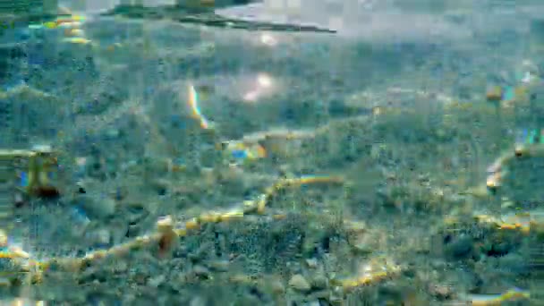 Yakın plan. Ege Denizi 'nin berrak sularının altında çok renkli küçük çakıl taşları görülebilir. Güneş ışığı, ışınlar suya yansıyor.. — Stok video