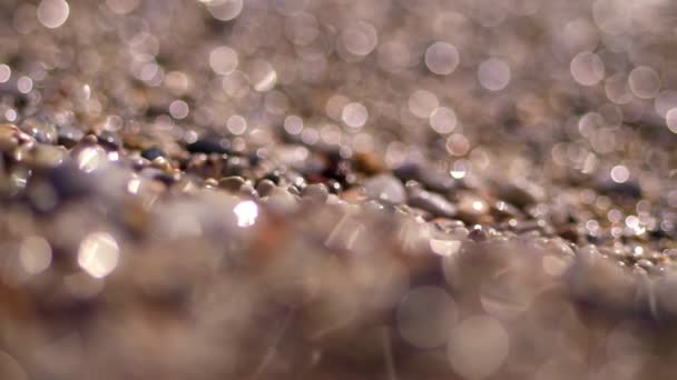 Enfoque borroso, muy cerca de piedras de mar redondas multicolores en la orilla y el reflejo de los rayos del sol, el resplandor. día soleado de verano. abstracción . — Vídeo de stock