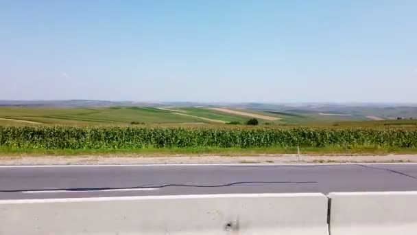 Carretera, autobahn, en el otro lado de la carretera son campos verdes. verano, día sin nubes. vista desde la ventana del coche en movimiento . — Vídeos de Stock