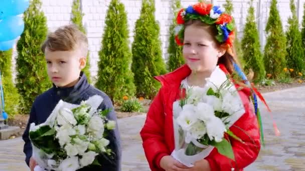 Cherkasy Region, Oekraïne, 10 oktober 2019: portret, kinderen van acht jaar, een jongen en een meisje met bloemenkrans op haar hoofd, boeketten staan en houden, buiten, bij winderig herfstweer. — Stockvideo