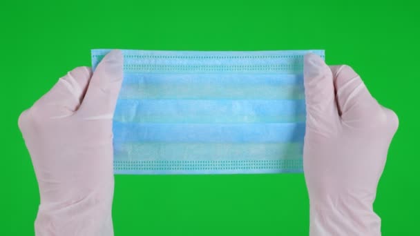 Крупным планом. руки в медицинских белых перчатках держать медицинский синий цвет маски для защиты от гриппа, респираторных заболеваний. на зеленом фоне — стоковое видео