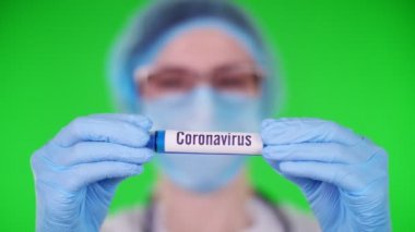yeşil arka plan. Yakın plan, doktorlar mavi tıbbi eldivenlerle ellerinde yazılı koronavirüsle test tüpü tutuyorlar. Tıbbi şapkalı, maskeli bir doktor. laboratuvar araştırma konsepti.
