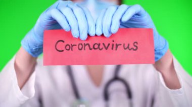 on a green background. closeup, doctors hands in blue medical gloves are tearing, tearing the coronavirus inscription on a red paper card. Concept of coronavirus quarantine. MERS-Cov. Novel