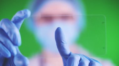 yeşil arka plan. Yakın plan, doktor tıbbi şapka, maske, mavi tıbbi eldiven, bir cam kart tutuyor ve tıklatıyor. reklam, metin veya videonun karta yerleştirilmesi mümkündür.