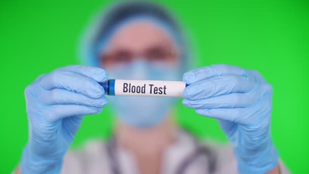 Green background. close-up, doctors hands in blue medical gloves holds test tube with inscription blood test. doctor wearing medical cap, mask. laboratory research concept. — Stock Video