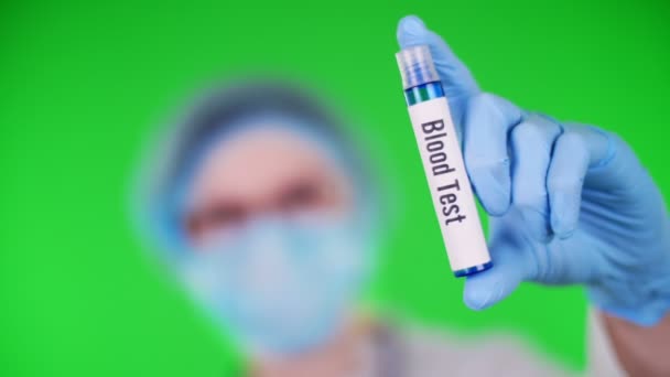 Zelené pozadí. zblízka, lékaři ruku v modré lékařské rukavici drží zkumavky s nápisem krevní testy. doktor v lékařské čepici, maska. koncepce laboratorního výzkumu — Stock video