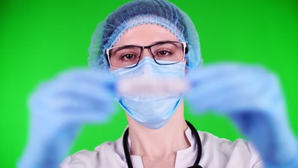 Yeşil arka plan. Yakın plan, doktorlar mavi tıbbi eldivenlerle ellerinde yazıt örneğiyle test tüpü tutuyorlar. Tıbbi şapkalı, maskeli bir doktor. laboratuvar araştırma konsepti. — Stok video