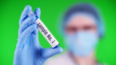 yeşil arka plan. Yakın plan, doktorlar mavi tıbbi eldiven veriyorlar ve üzerinde örnek yazılar olan test tüpü tutuyorlar. Tıbbi şapkalı, maskeli bir doktor. laboratuvar araştırma konsepti