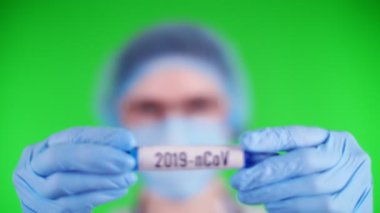 yeşil arka plan. Yakın plan, doktorlar mavi tıbbi eldivenleri elinde 2019 ncov yazısıyla test tüpü tutuyor. Tıbbi şapkalı, maskeli bir doktor. laboratuvar araştırma konsepti.
