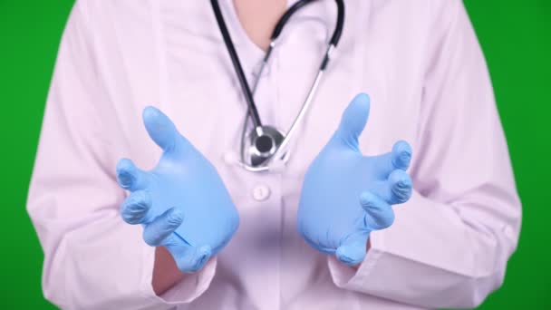 Close-up, médico vestido com uniforme médico branco, com um estetoscópio, segurando algo com as mãos em um fundo verde. é possível colocar um anúncio, texto ou vídeo . — Vídeo de Stock