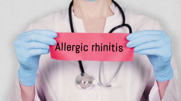 Nahaufnahme, Hände in blauen Medizinhandschuhen halten und reißen rote Papierkarten mit der Aufschrift Allergische Rhinitis. Arzt in weißer Arztuniform hat ein Stethoskop. — Stockvideo