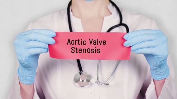 Nahaufnahme, Hände in blauen Medizinhandschuhen halten und reißen eine rote Papierkarte mit der Aufschrift Aortenklappenstenose. Arzt in weißer Arztuniform hat ein Stethoskop. — Stockvideo
