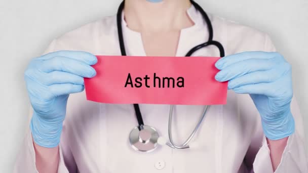Close-up, handen in blauw medische handschoenen houden en scheuren rode papieren kaart met een inscriptie astma. arts gekleed in wit medisch uniform, heeft een stethoscoop. — Stockvideo