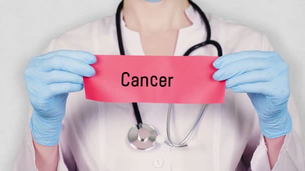 Closeup, hands in blue medical gloves hold and tear red paper card with an inscription cancer cancer . doctor dressed in white medical uniform, has a stethoscope. — Stock Video